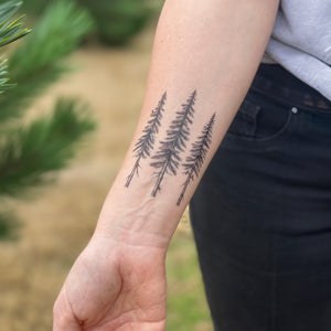 persons laying both forearms out showing a temporary tattoo on each arm, a pine tree design and a cardinal bird