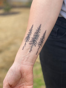persons laying both forearms out showing a temporary tattoo on each arm, a pine tree design and a cardinal bird