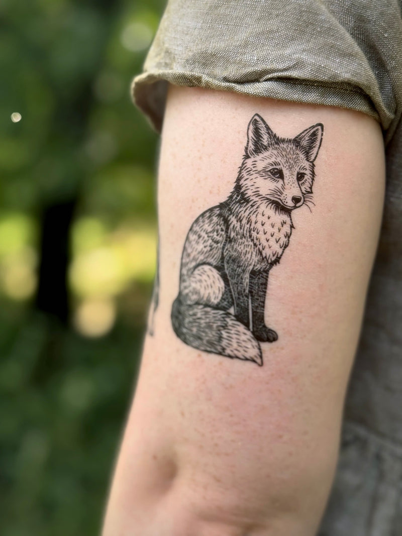 Temporary Tattoo of a fox on a person's arm in a green dress with a blurred natural background