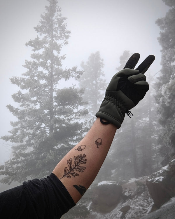 Person wearing a black glove with a temporary tattooed arm against a forest background