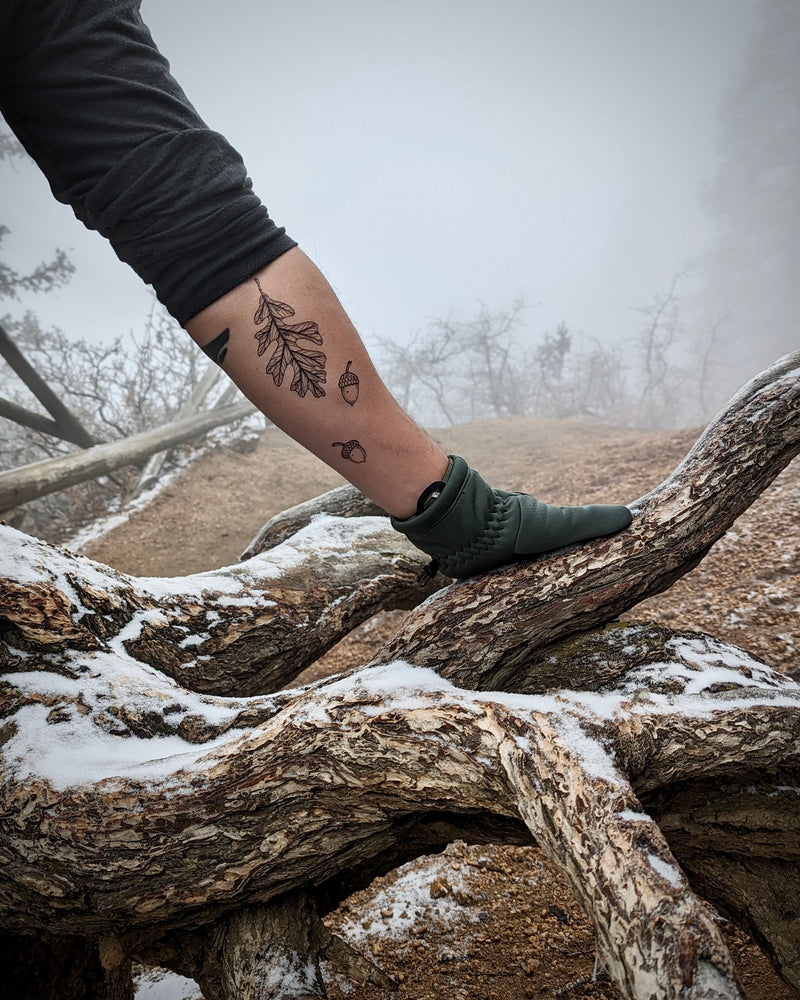 Person with a temporary tattoo on their arm standing on a snow-covered branch in a foggy landscape.