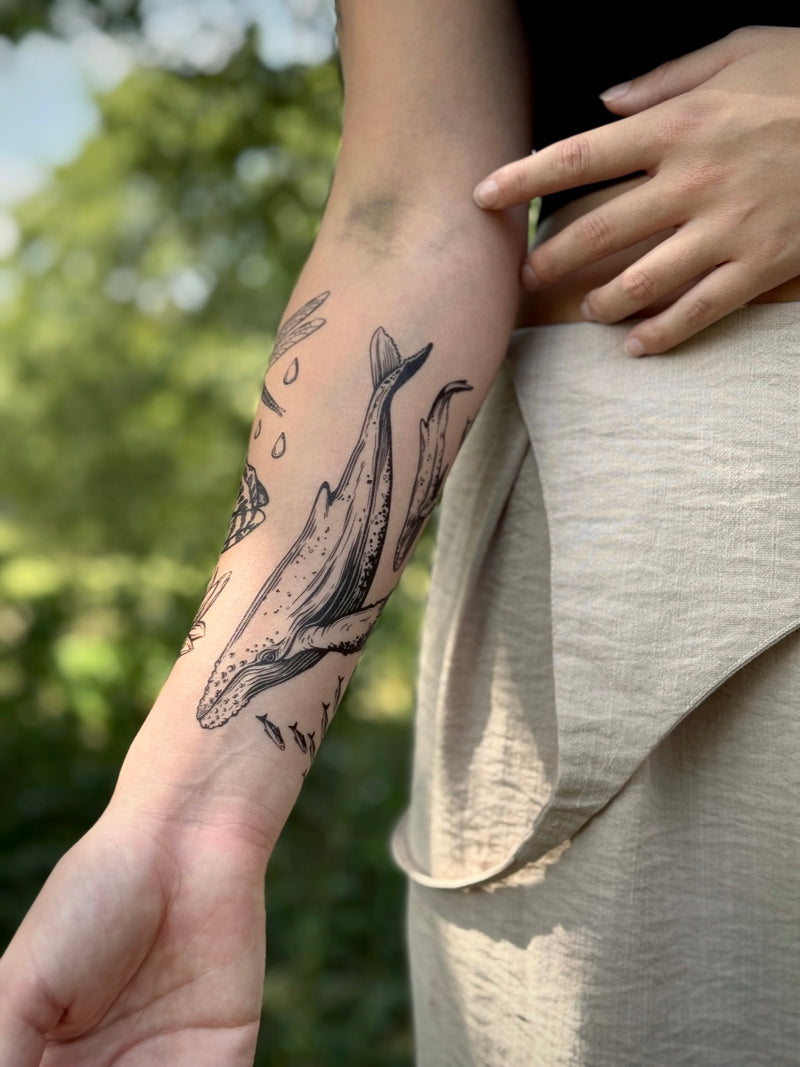 Person with a whale temporary tattoo on their arm, standing outdoors with greenery in the background.