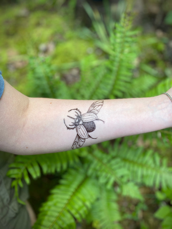 Rhinoceros beetle temporary tattoo on persons arm in a green blurred nature background 
