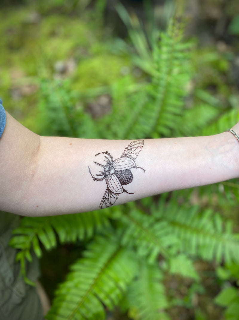 Rhinoceros beetle temporary tattoo on persons arm in a green blurred nature background 