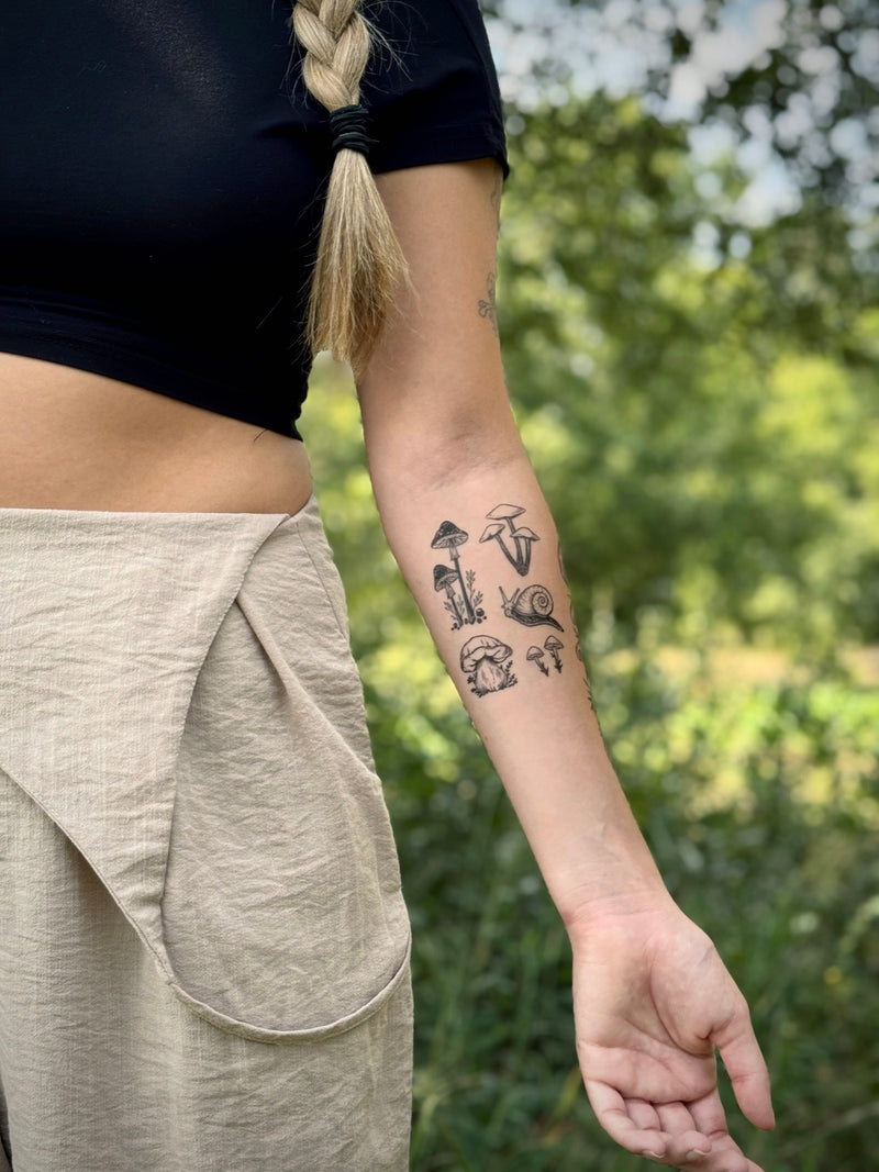 Person with tiny mushroom temporary  tattoos on arm wearing black and cream in blurred nature background 