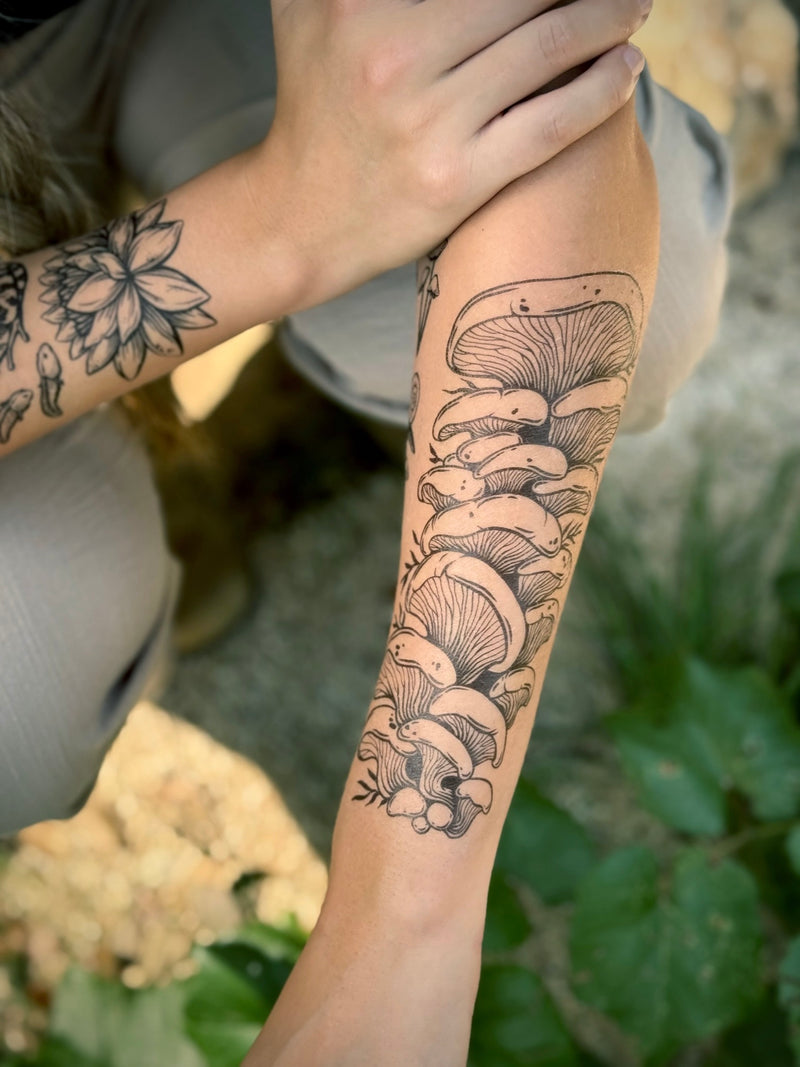 Person with a detailed mushroom temporary tattoo on their arm, standing outdoors.