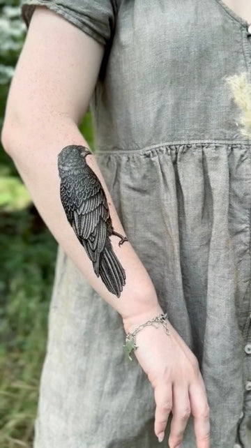 Person wearing a detailed bird temporary tattoo on their arm, dressed in a gray dress.