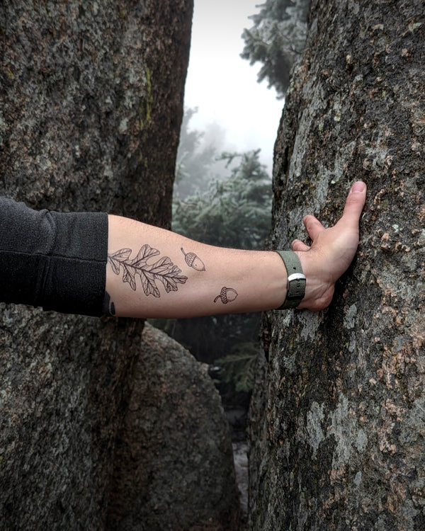 Person with arm temporary tattoos holding onto a tree in a forest setting