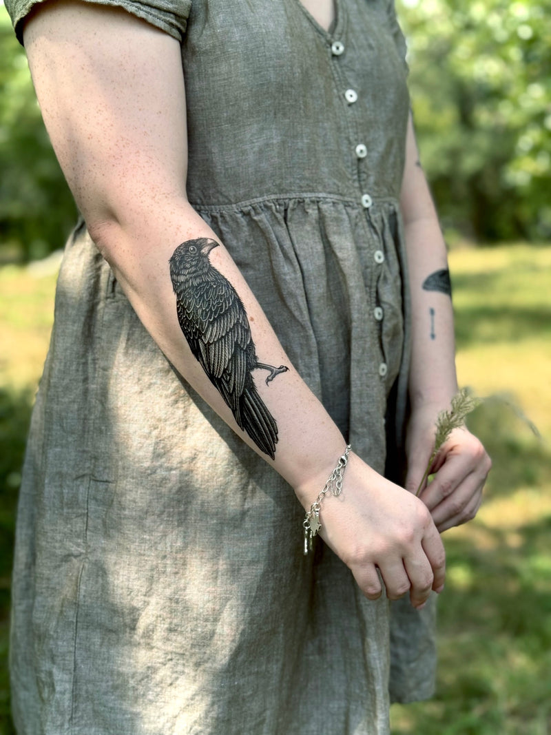 Person wearing a green dress with a bird temporary tattoo on their arm, standing outdoors.