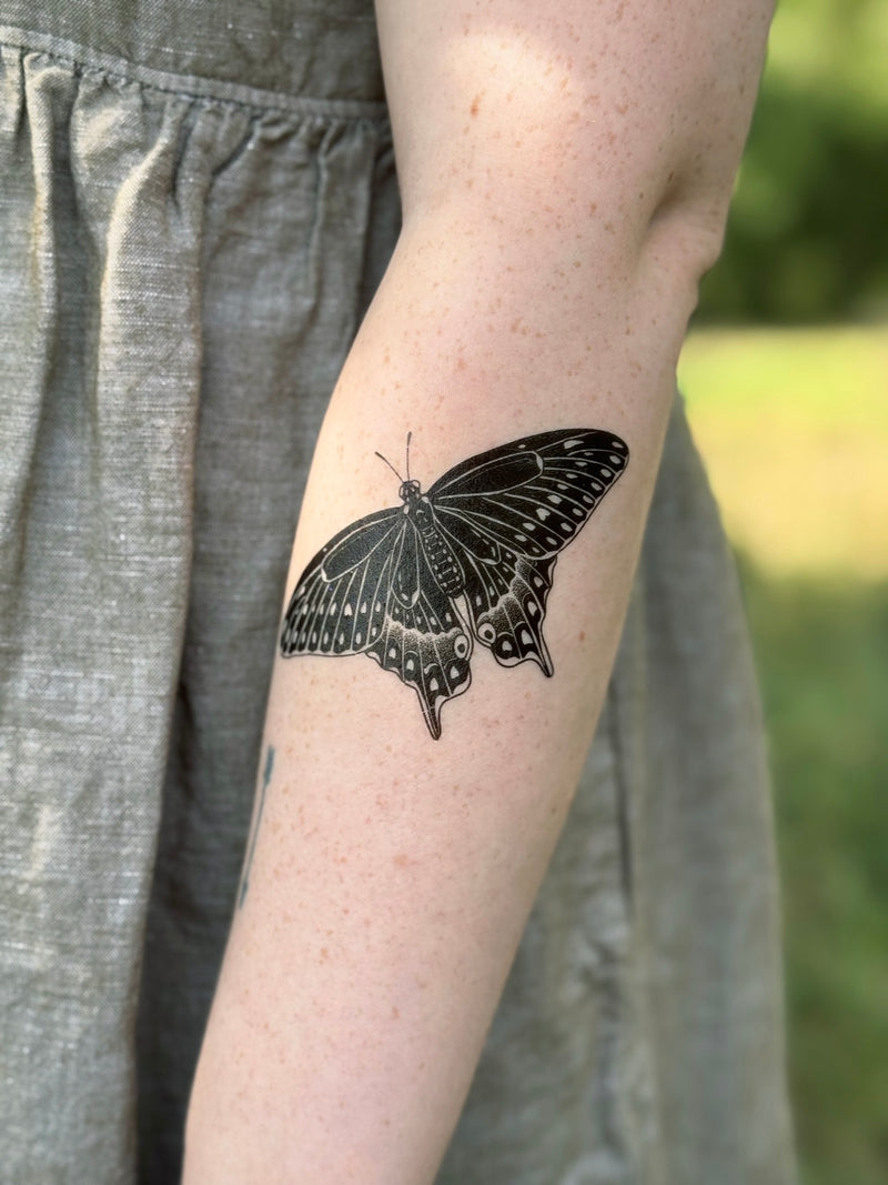 swallowtail butterfly temporary tattoo on a person's arm with a blurred natural background