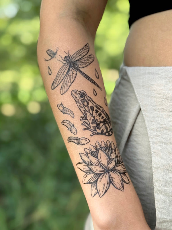 temporary Tattoo of a dragonfly, frog, and lotus flower on a person's arm with a blurred green background.