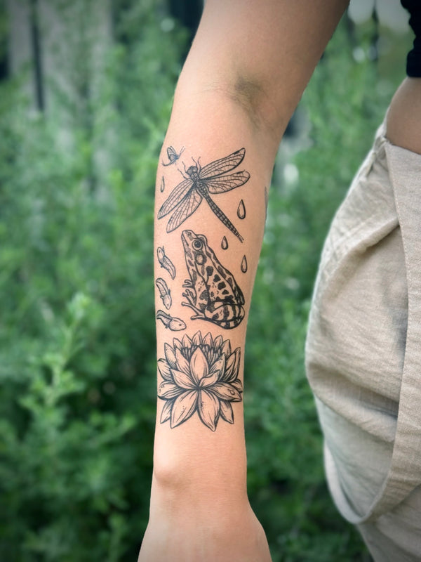temporary Tattoo of a frog, dragonfly, and lotus flower on a person's arm with a blurred green background.