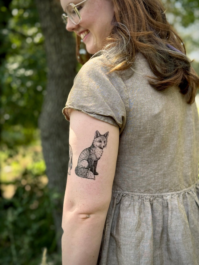 Woman wearing a gray dress with a fox temporary tattoo on her arm, standing outdoors.