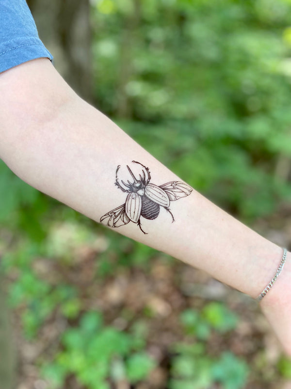 Rhinoceros beetle temporary tattoo on persons arm wearing blue with a blurred nature background 