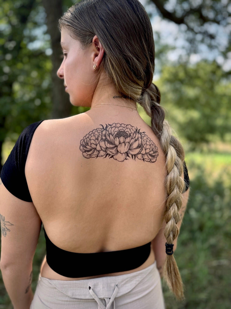 Woman with a peony temporary tattoo on her back standing outdoors with trees in the background