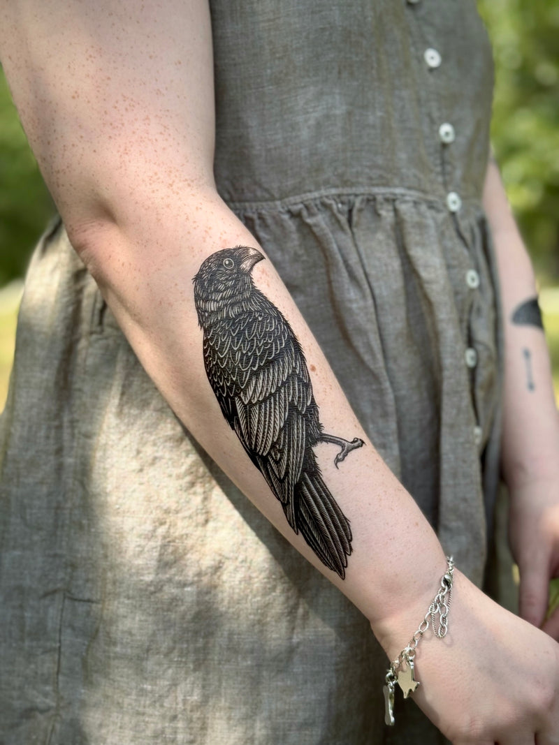 Person wearing a gray dress with a detailed black bird temporary tattoo on their arm.