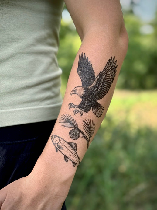 Tattoo of an eagle and fish on a person's arm with a blurred green background