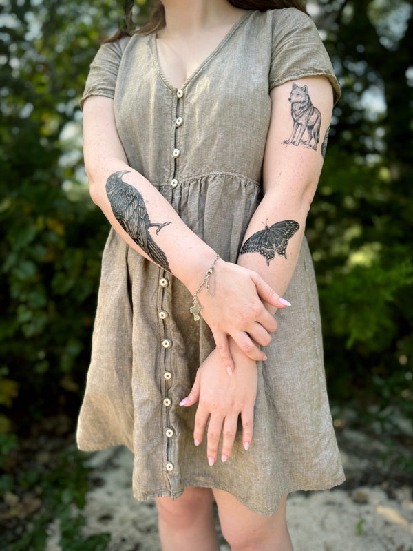 Person wearing a green dress with visible 
 temporary tattoos on arms against a natural background