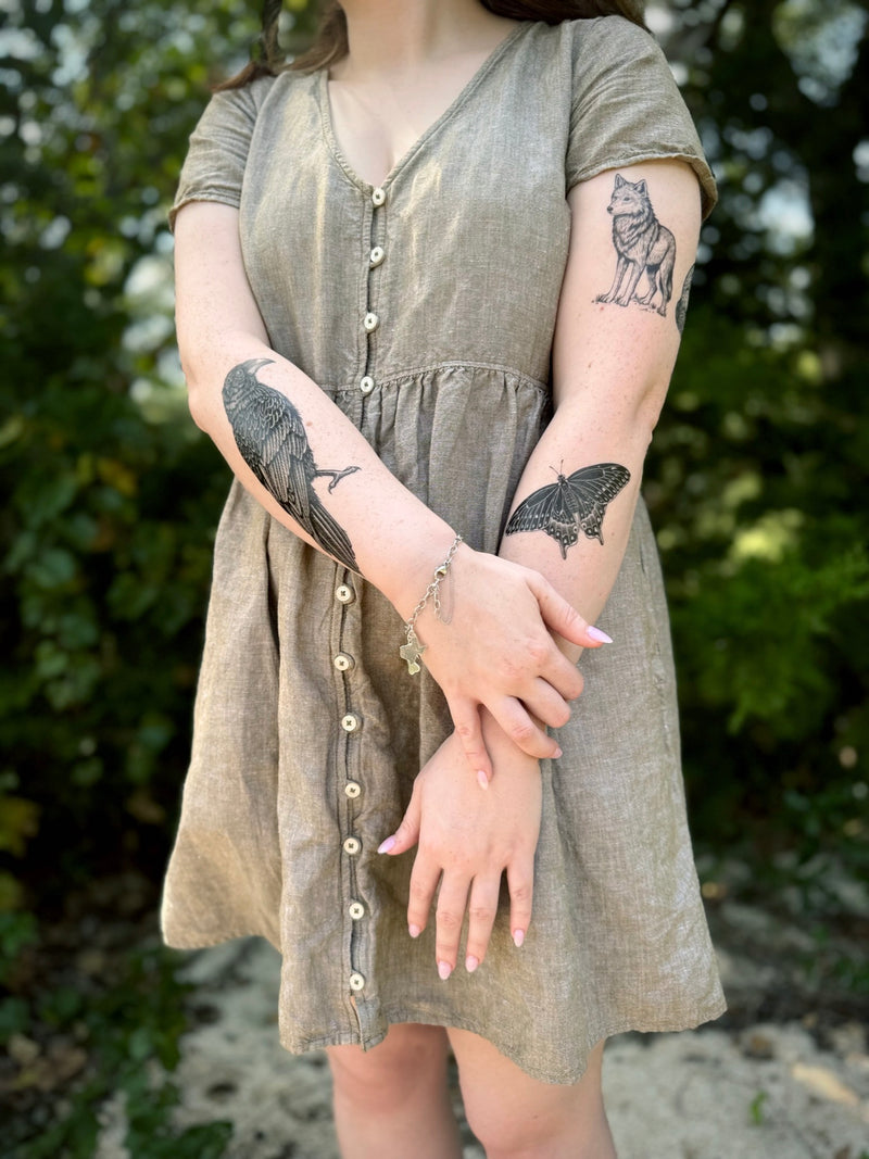 Person wearing a green dress with visible 
 temporary tattoos on arms against a natural background