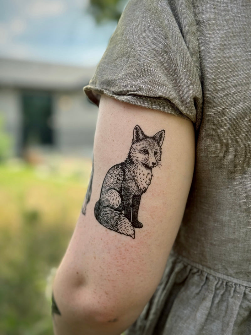 Temporary Tattoo of a fox on a person's arm in a grey dress with a blurred outdoor background