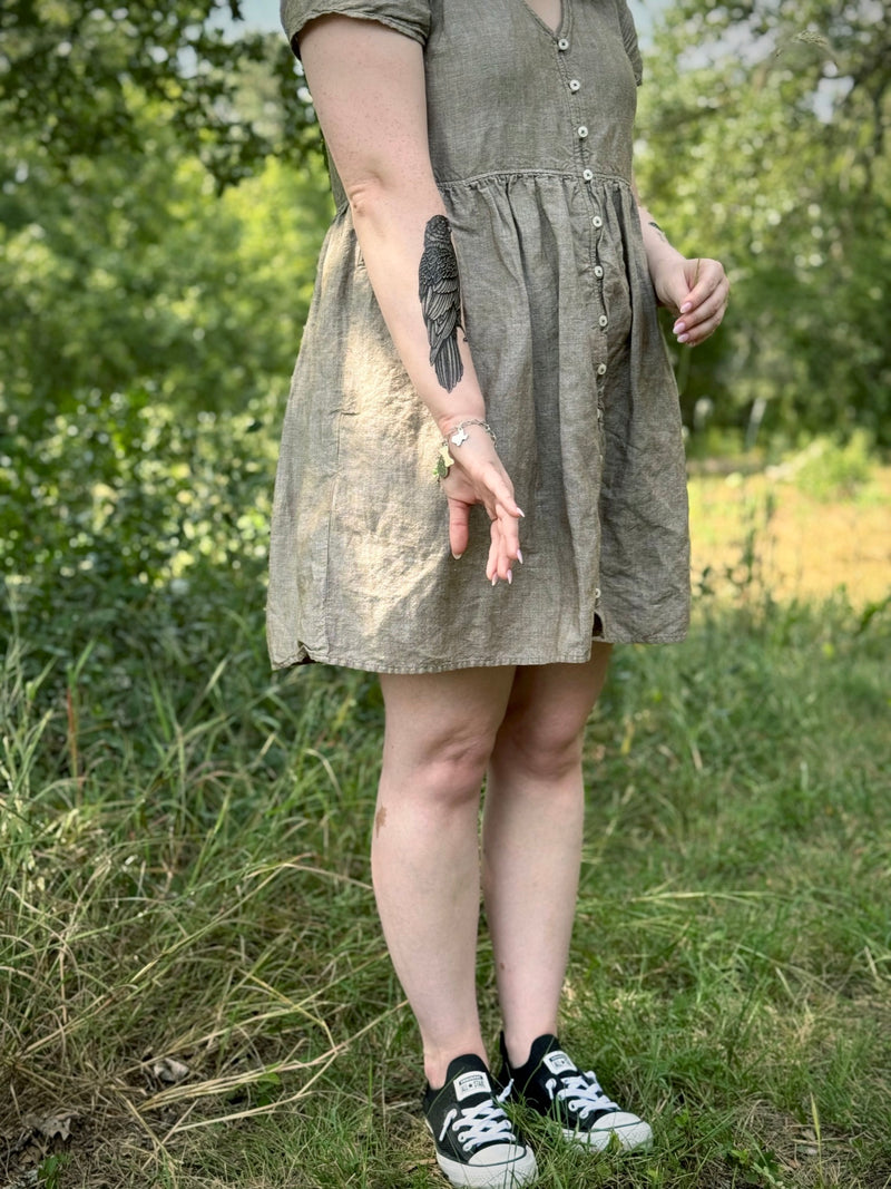 Person wearing a green dress standing in a grassy outdoor area with raven temporary tattoo on arm