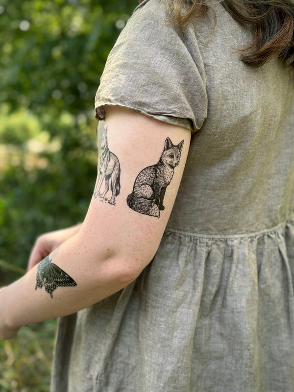 Person wearing a gray dress with temporary tattoos on their arm against a blurred green background