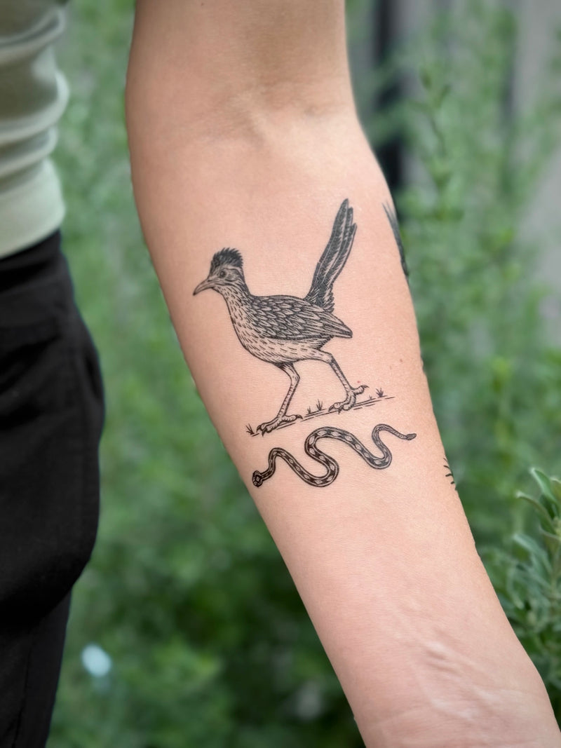 Temporary Tattoo of a roadrunner and snake design on a person's arm with a blurred green background
