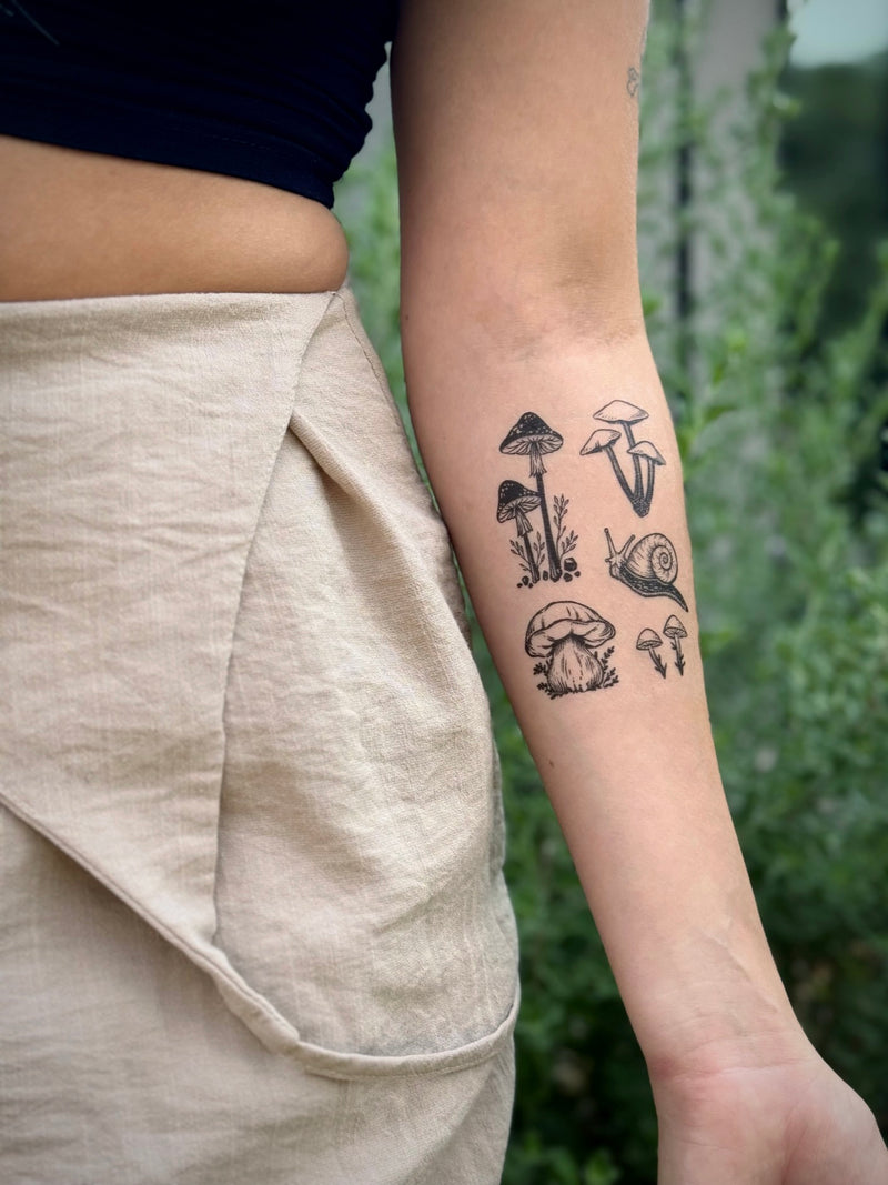 Person with black mushroom temporary tattoos on their arm against a blurred green background