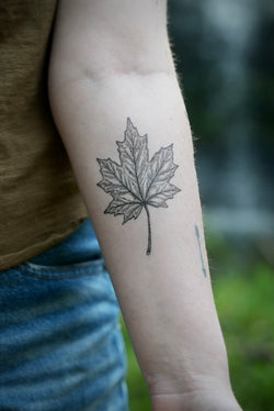 person wearing black ink temporary tattoo of a maple leaf in their forearm