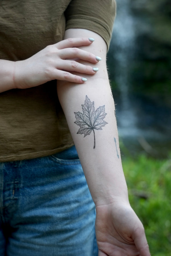 person wearing black ink temporary tattoo of a maple leaf in their forearm