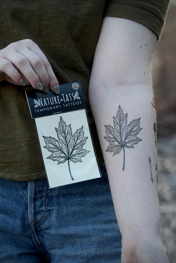 person wearing black ink temporary tattoo of a maple leaf in their forearm and holding a packaged temporary tattoo by naturetats of the same maple leaf