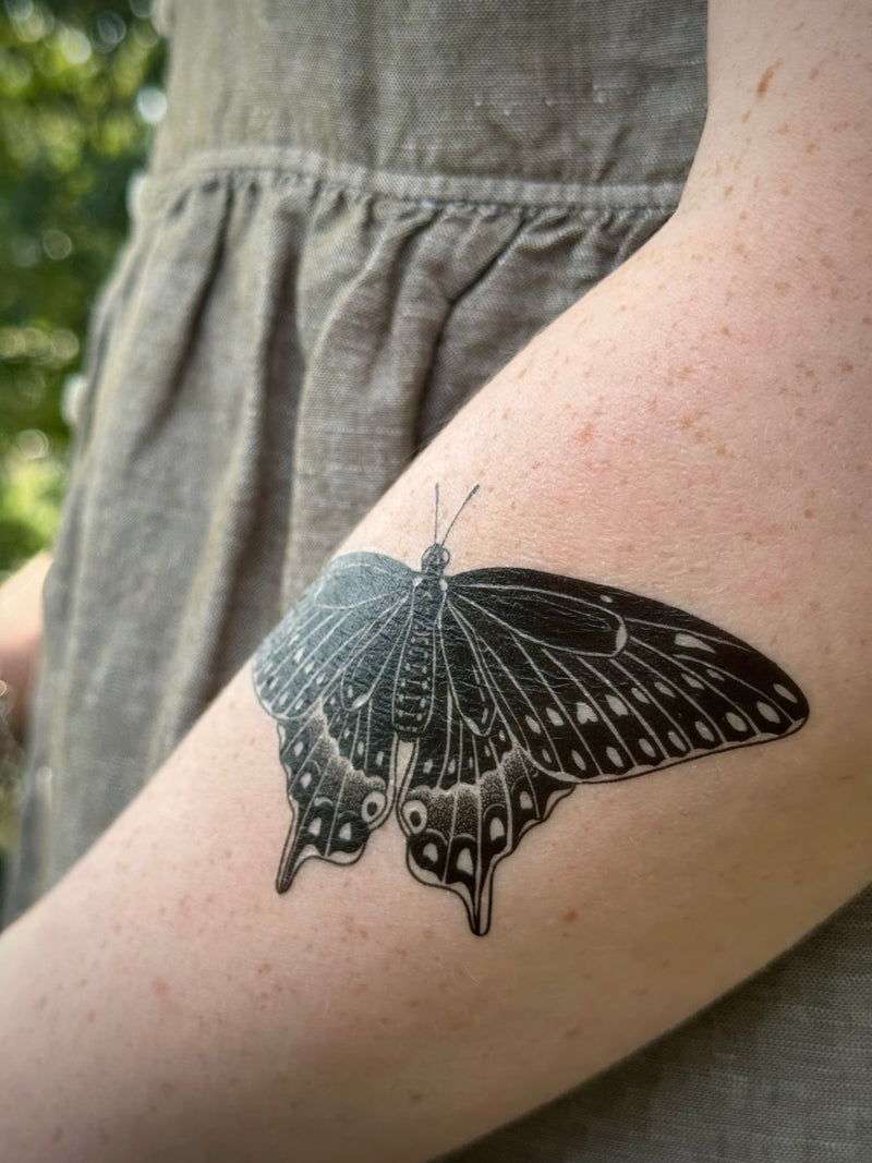 Black butterfly temporary tattoo on a person's arm with a blurred background