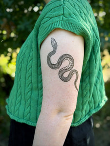 Person wearing a green sweater with a snake tattoo on their arm.