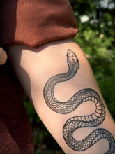 Snake tattoo on a person's arm with a blurred natural background