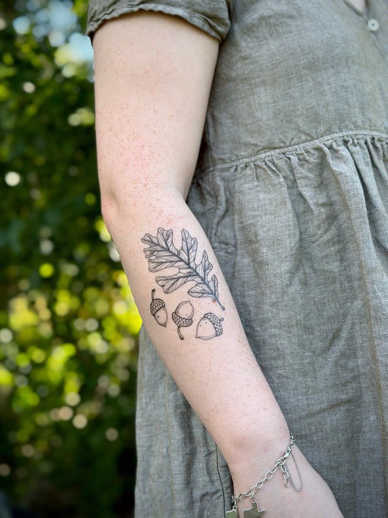 Person wearing a gray dress with a nature-themed temporary tattoo on their arm, standing outdoors.
