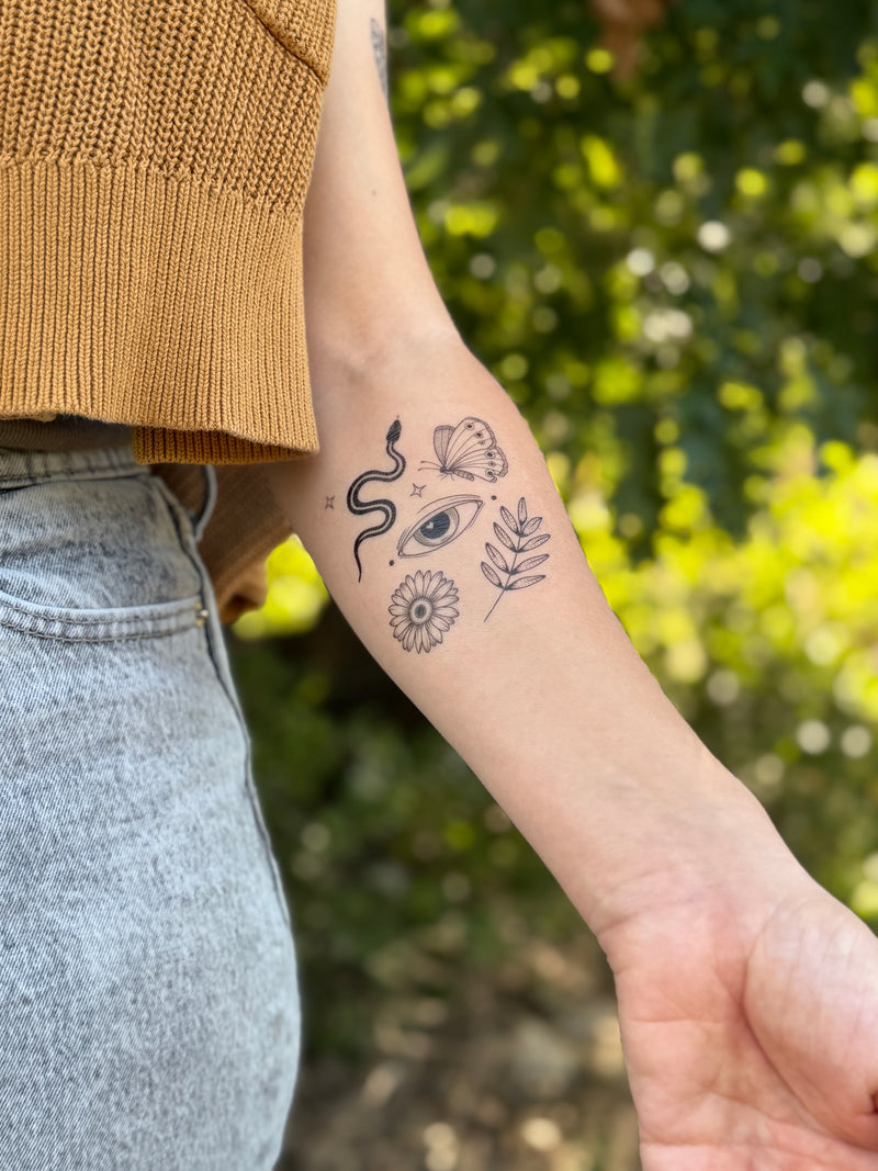Person wearing a sleeve with various temporary tattoos against a blurred natural background 