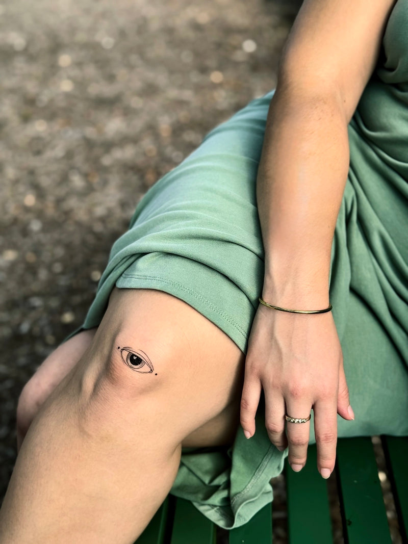 Person wearing a green dress with a small temporary tattoo on their knee, sitting on a bench.