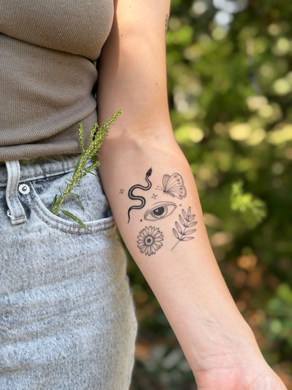 Person with a temporary tattoo on their arm featuring an eye, butterfly, and floral elements, standing outdoors.