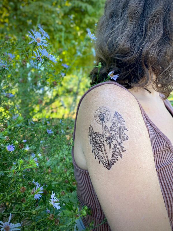Dandelion temporary tattoo on shoulder with a green floral background 