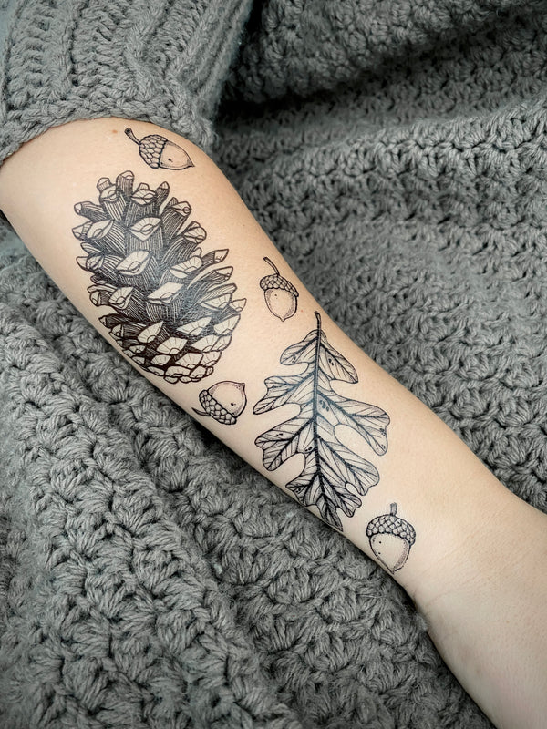 Temporary Tattoos of pine cones and acorns on a person's arm against a textured gray background