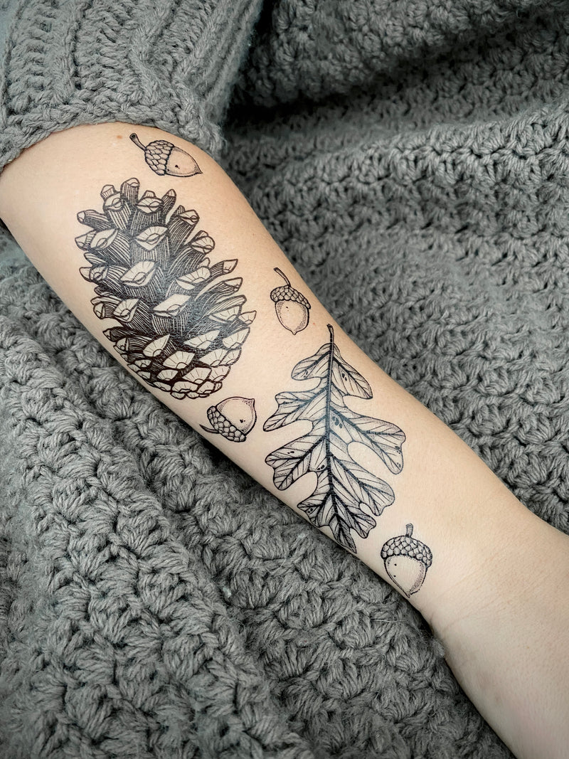 Temporary Tattoos of pine cones and acorns on a person's arm against a textured gray background