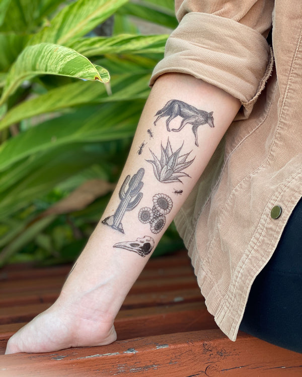 desert wild temporary tattoo on inside of arm with a brown wood and green leaf background 
