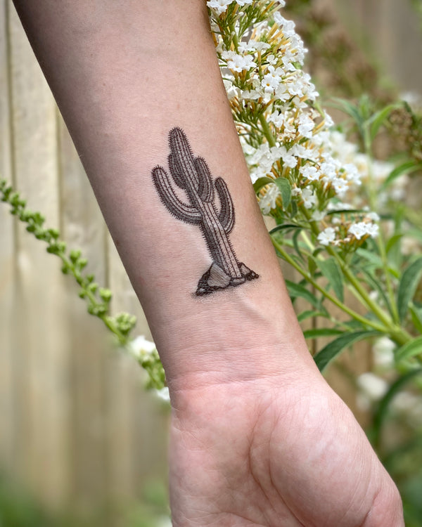 cactus temporary tattoo on wrist with a blurred floral background 