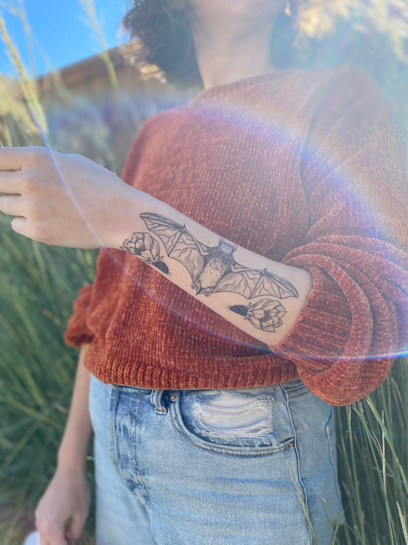 free-tailed bat temporary tattoo on persons arm wearing orange sweater and blue jeans in a nature background 