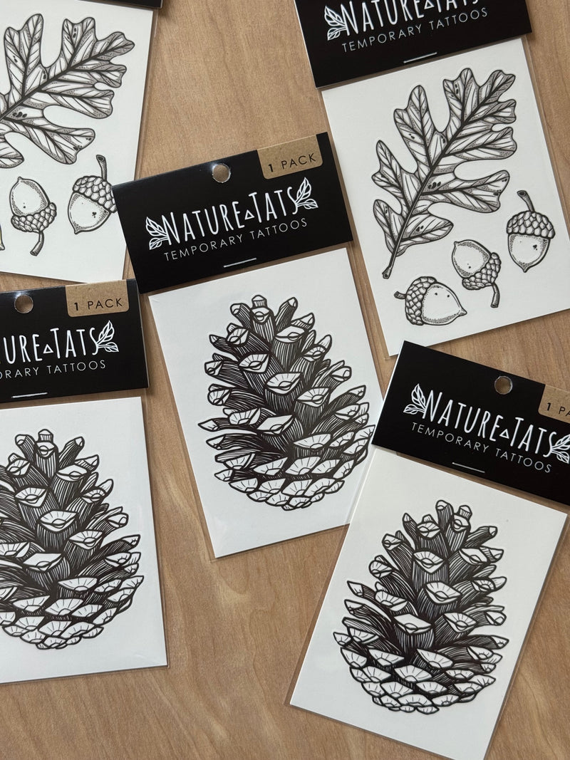 Nature-themed temporary tattoos with pinecones and acorns on white paper, displayed on a wooden surface.