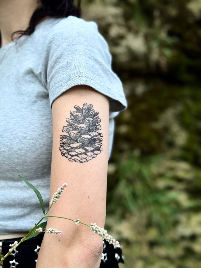 Person with a temporary tattoo of a pine cone on their arm, standing outdoors.