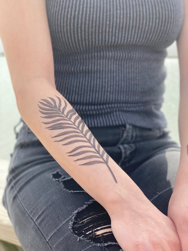 palm leaf temporary tattoo on persons arm wearing grey and black in blurred background 