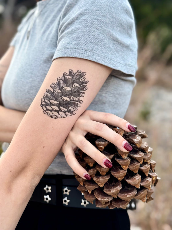 Person holding a pine cone with a pine cone temporary tattoo on their arm.