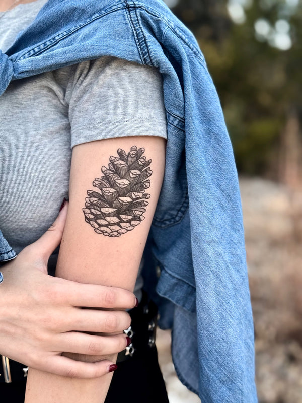 Person wearing a denim jacket with a pine cone temporary tattoo on their arm.