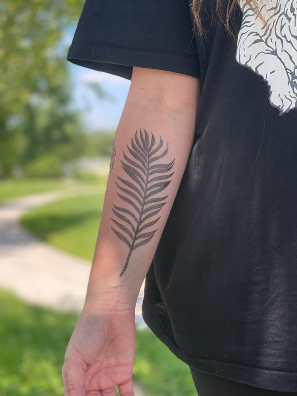 palm leaf temporary tattoo on persons arm wearing black in a blurred nature background 